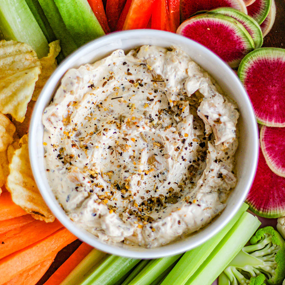 Closeup photo of a bowl of onion dip surrounded by fresh vegetables.