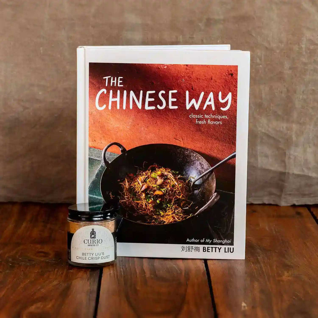 Cookbook The Chinese Way by Betty Liu next to a glass jar of Betty Liu's Chile Crisp Dust, a collaboration blend with Curio Spice.