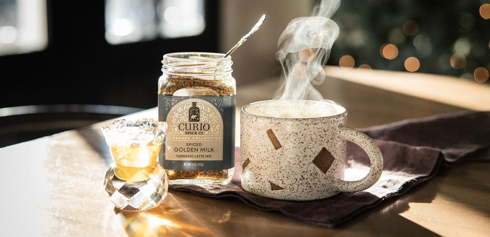 Jar of 'Curio & Company' golden milk with a steaming cup on a wooden surface.