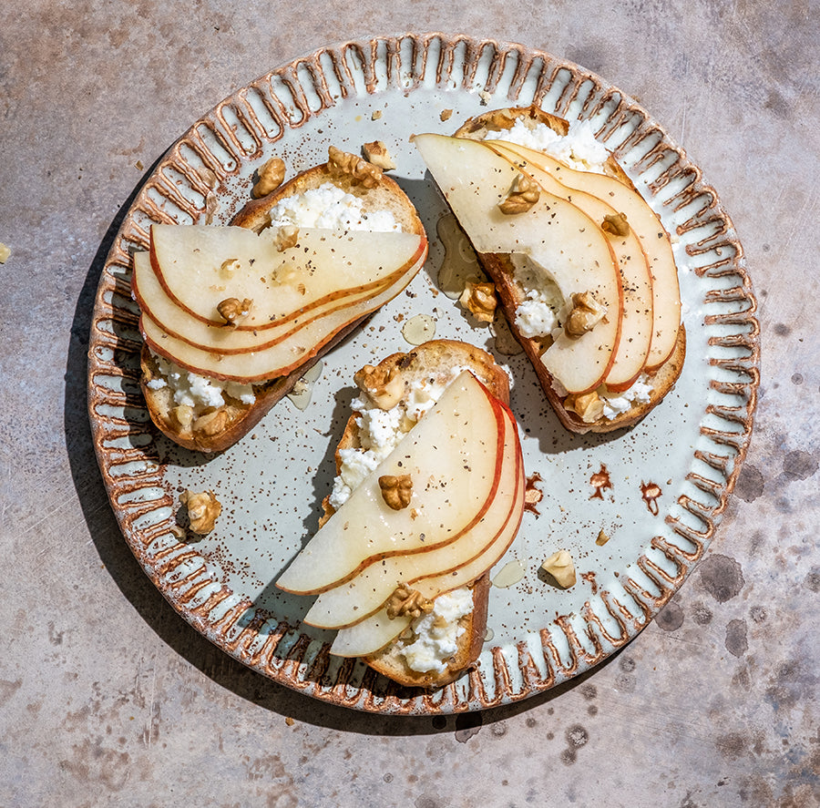 Three pieces toast with cheese spread and pears on decorative plate.