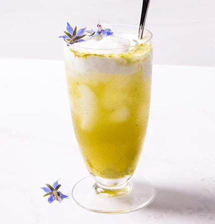 Tall glass footed glass with iced pandan dirty soda and blue edible flowers.