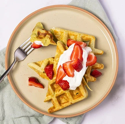 Plate of crispy pandan waffles topped with whipped cream and strawberries.