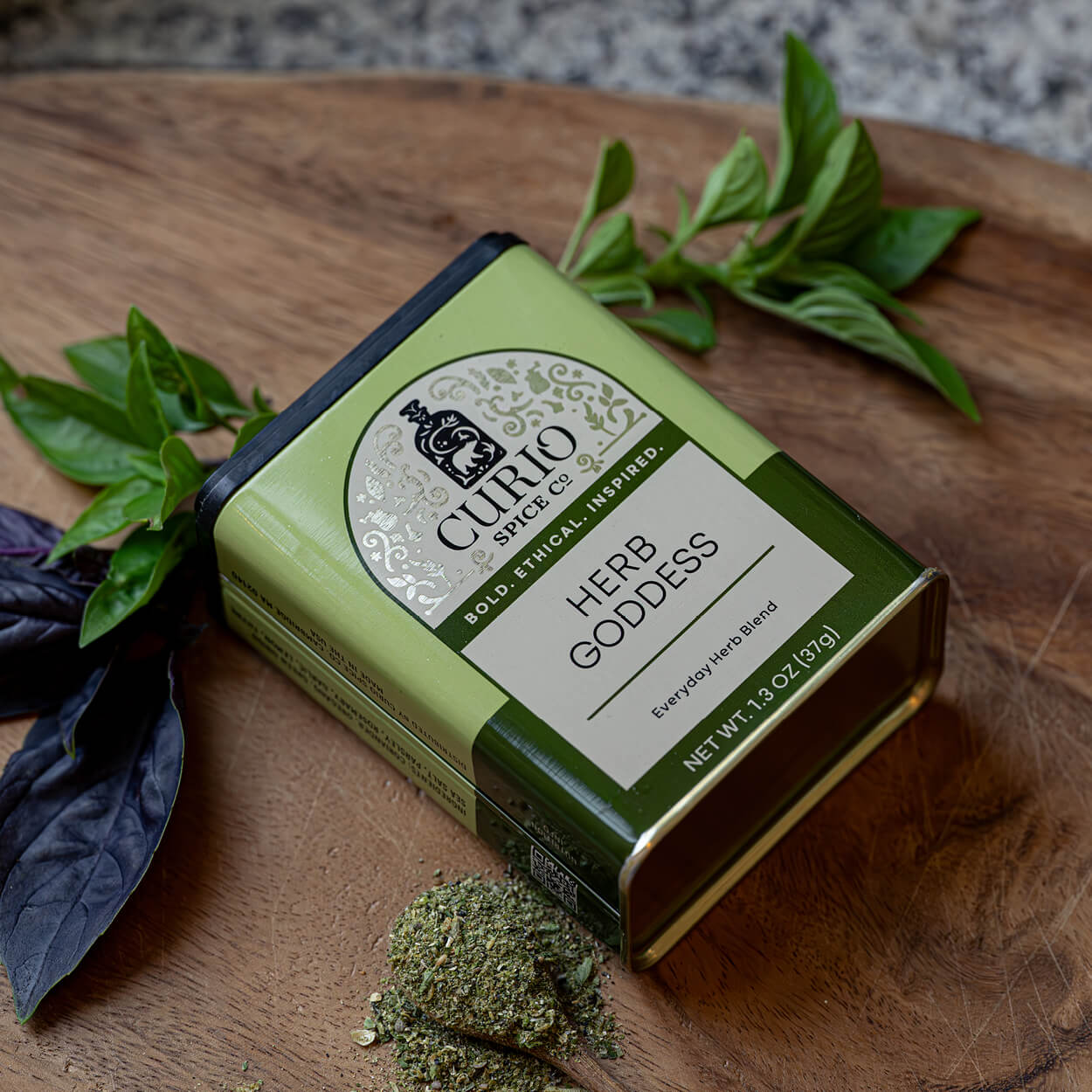 Curio Spice Co. Herb Goddess spice blend packaging on a wooden surface with herbs.