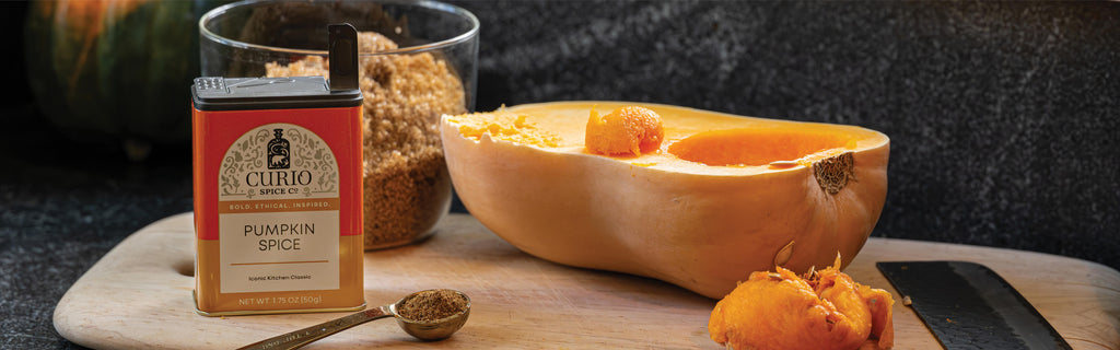 Curio pumpkin spice box with a halved pumpkin and spoon on a wooden board.