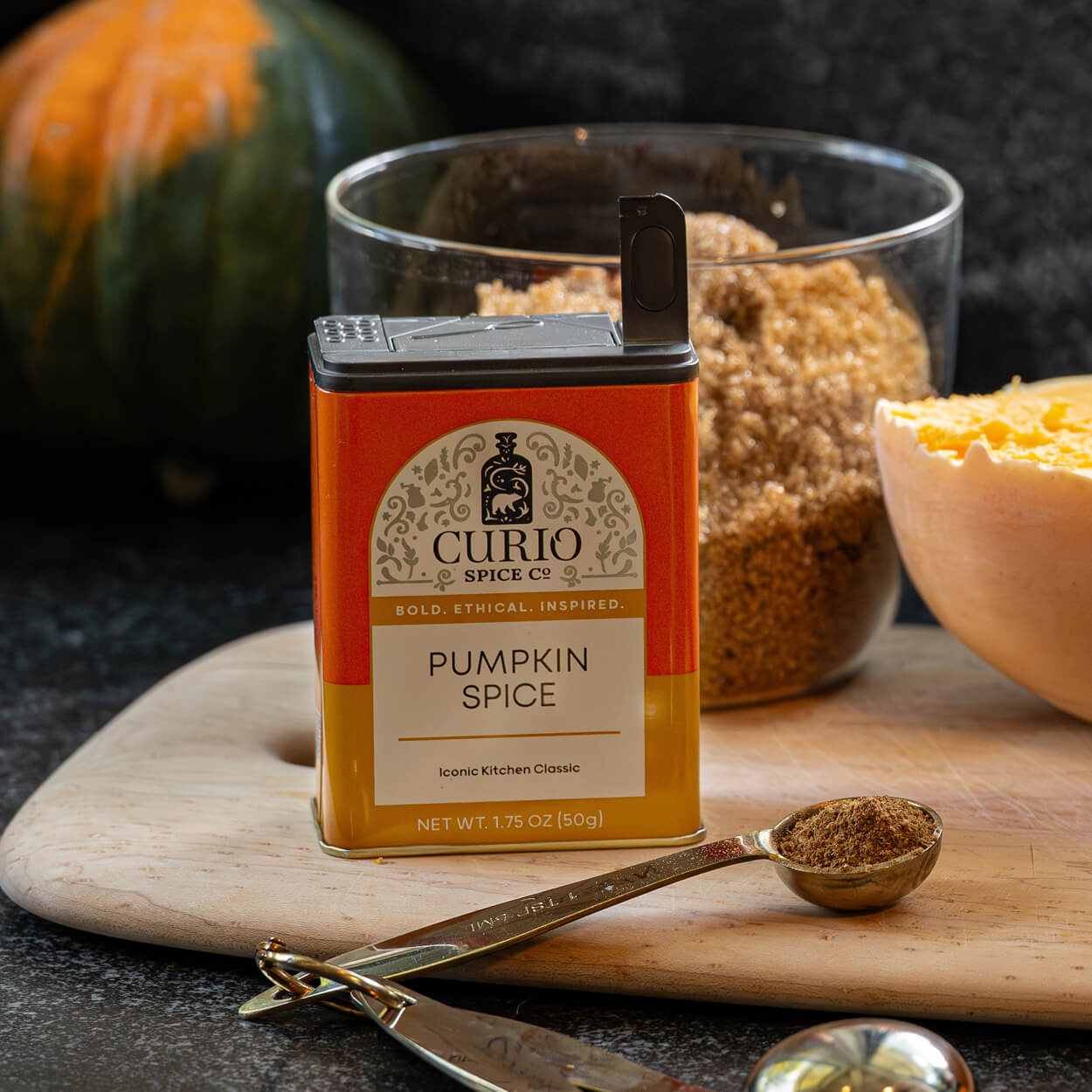 Curio Spice Co. pumpkin spice container on a wooden board with pumpkins and a spoonful of spice.