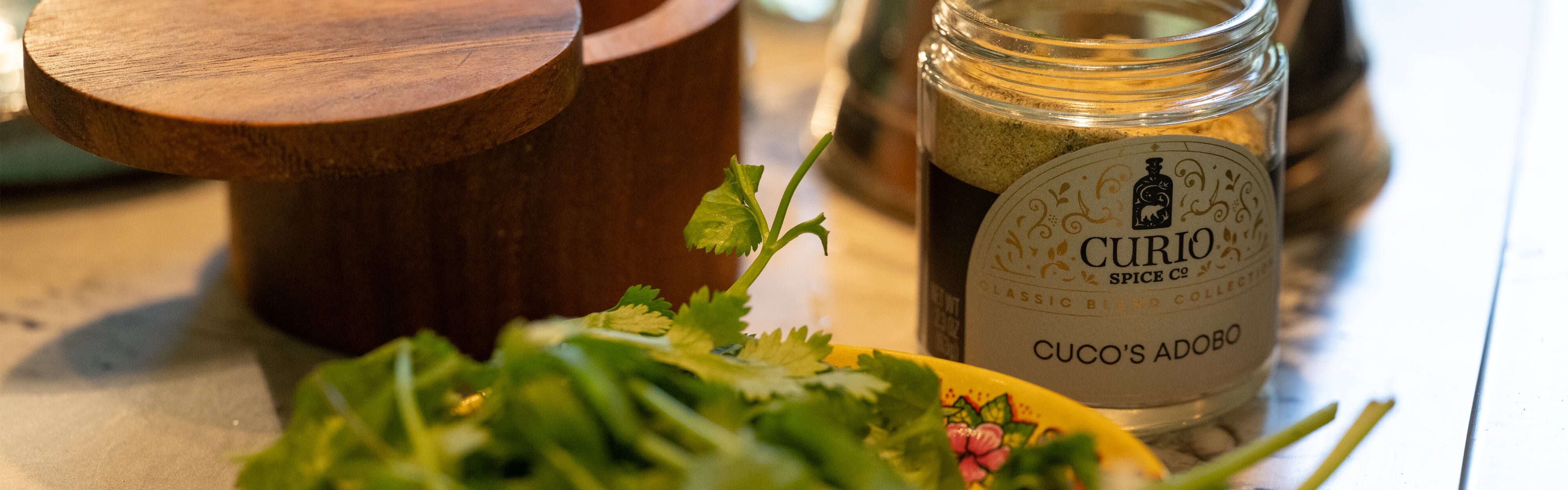 Jar of Curio Spice Co. adobo seasoning on a table with herbs