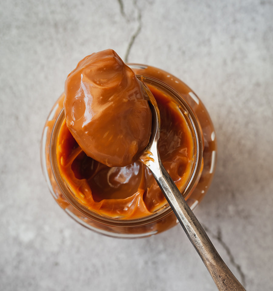 Jar of dulce de leche with a spoon lifting a scoop out, on a light gray background