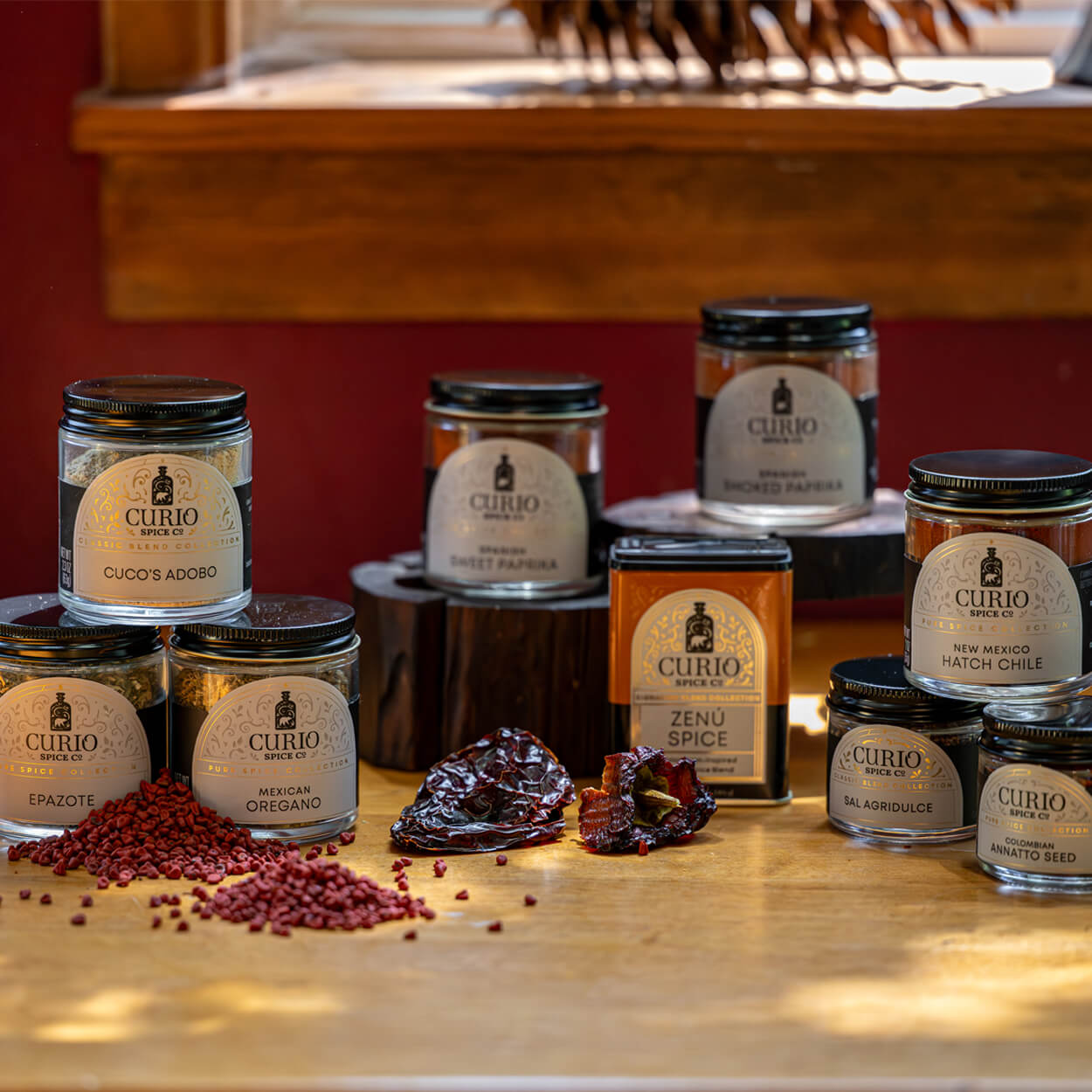 Assorted jars of Curio Spice Co. products on a wooden surface with a red wall in the background.