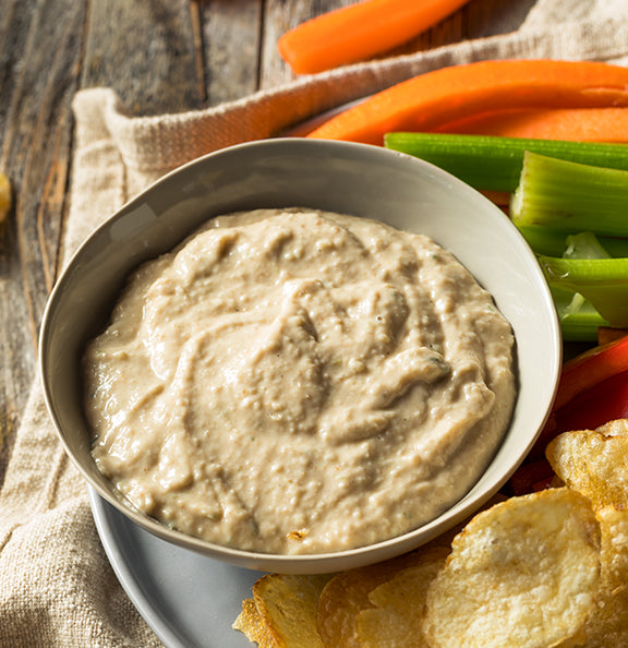 Bowl of creamy onion dip with vegetables and chips on a wooden surface