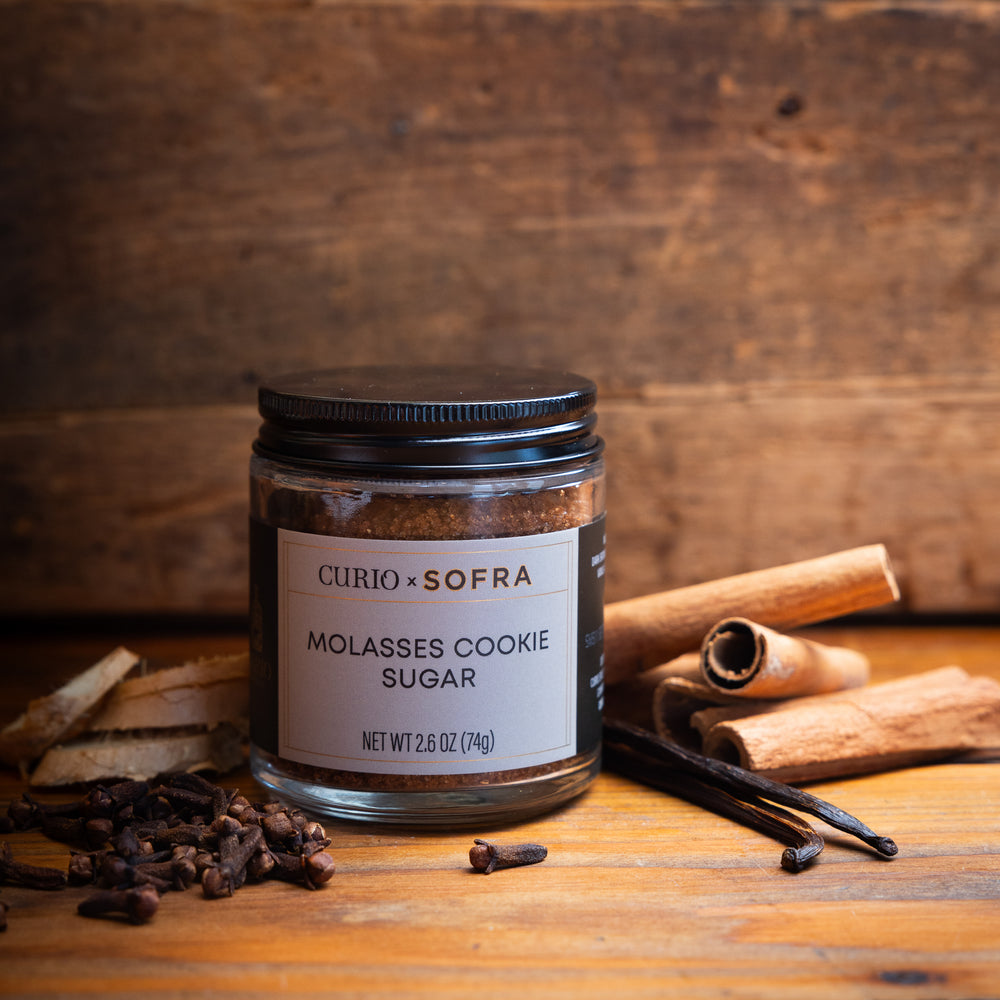 Jar of Curio Sofra Molasses Cookie Sugar with cinnamon sticks and vanilla beans on a wooden surface.