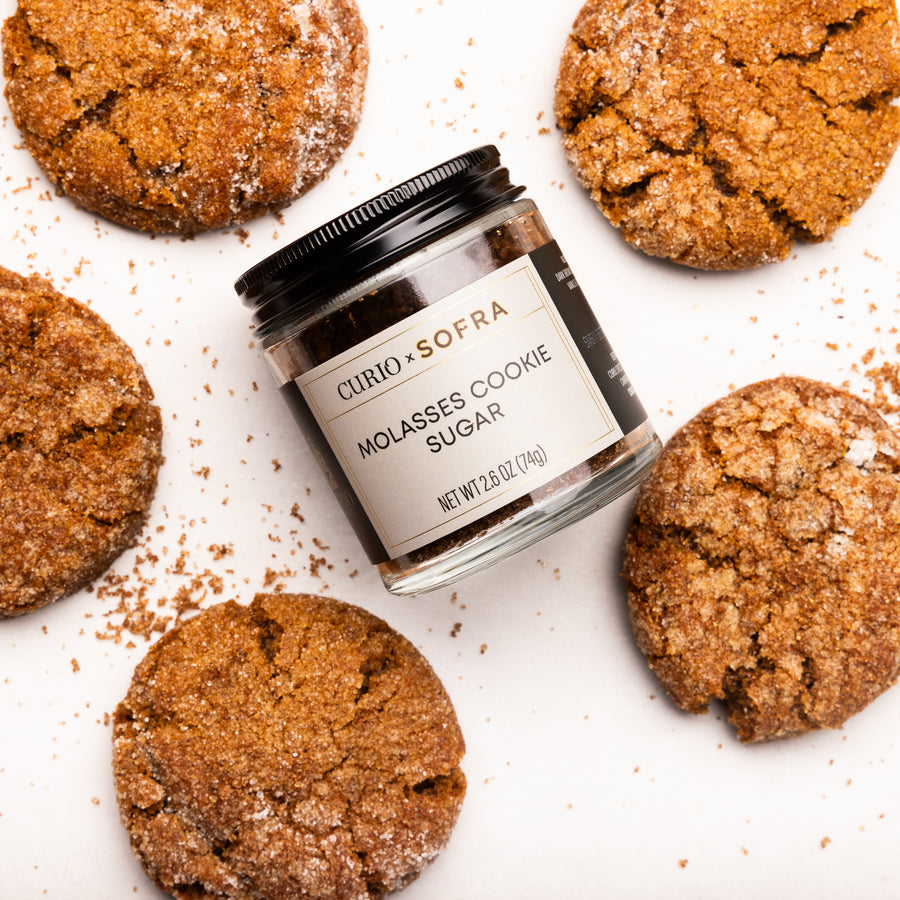 Jar of Curio & Sofra Molasses Cookie Sugar surrounded by cookies on a white background