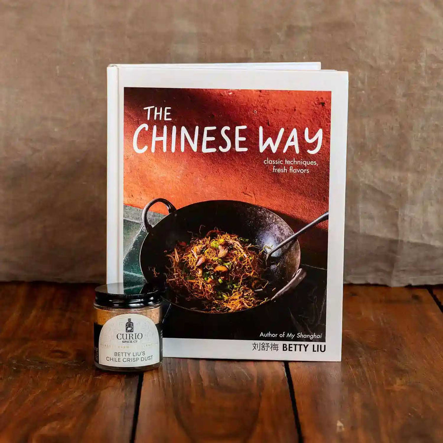 Cookbook The Chinese Way by Betty Liu next to a glass jar of Betty Liu's Chile Crisp Dust, a collaboration blend with Curio Spice.