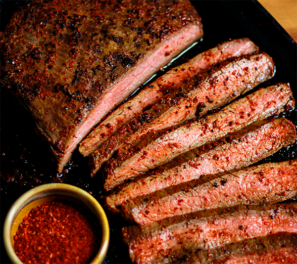 Sliced steak on a plate with a side of Curio's Magic Salt chile blend.