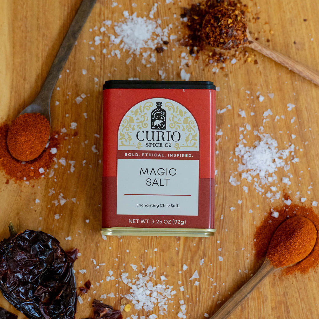 Curio Magic Salt packaging on a wooden surface with spices and a spoon.