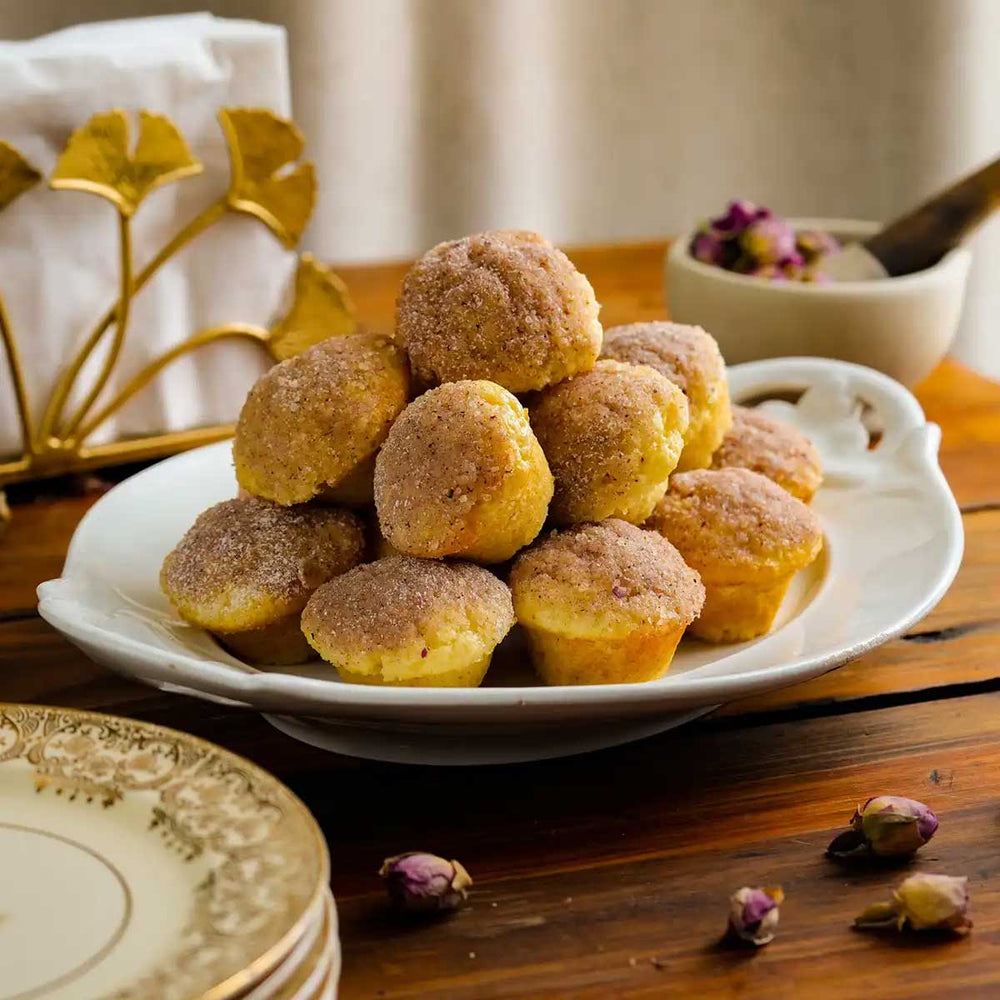 A pile of rose-sugared donuts on a white plate sitting on top of a wooden table with floral accents.