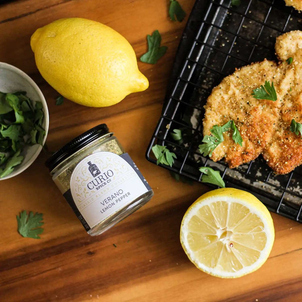 Verano Lemon Pepper sitting next to a chicken cutlet, lemons, and herbs