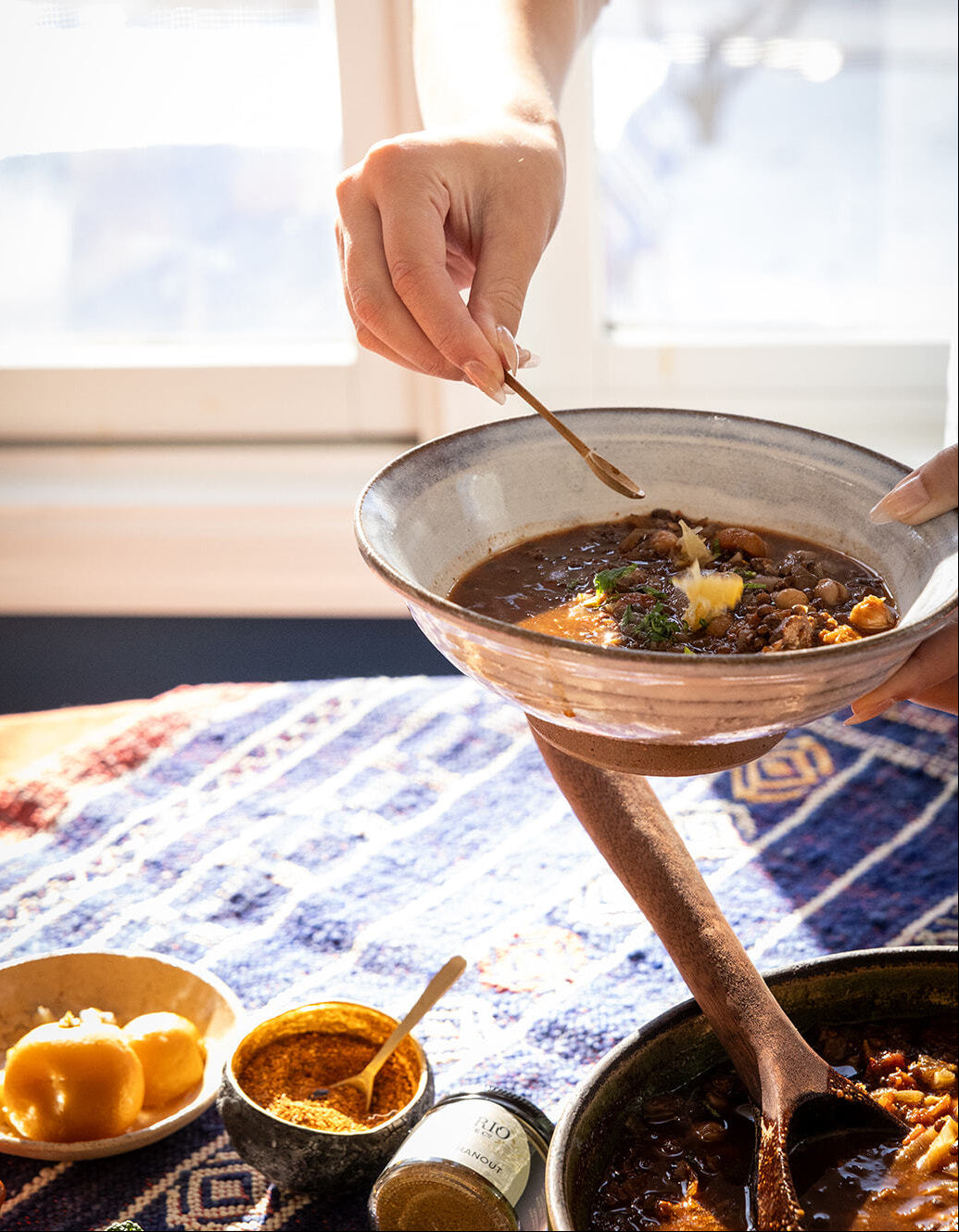 Person holding a bowl of soup with a spoon, sitting on a patterned blanket.
