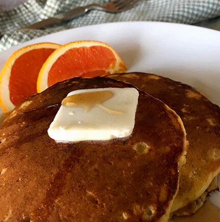 Stack of pancakes with butter and orange slices on a plate.
