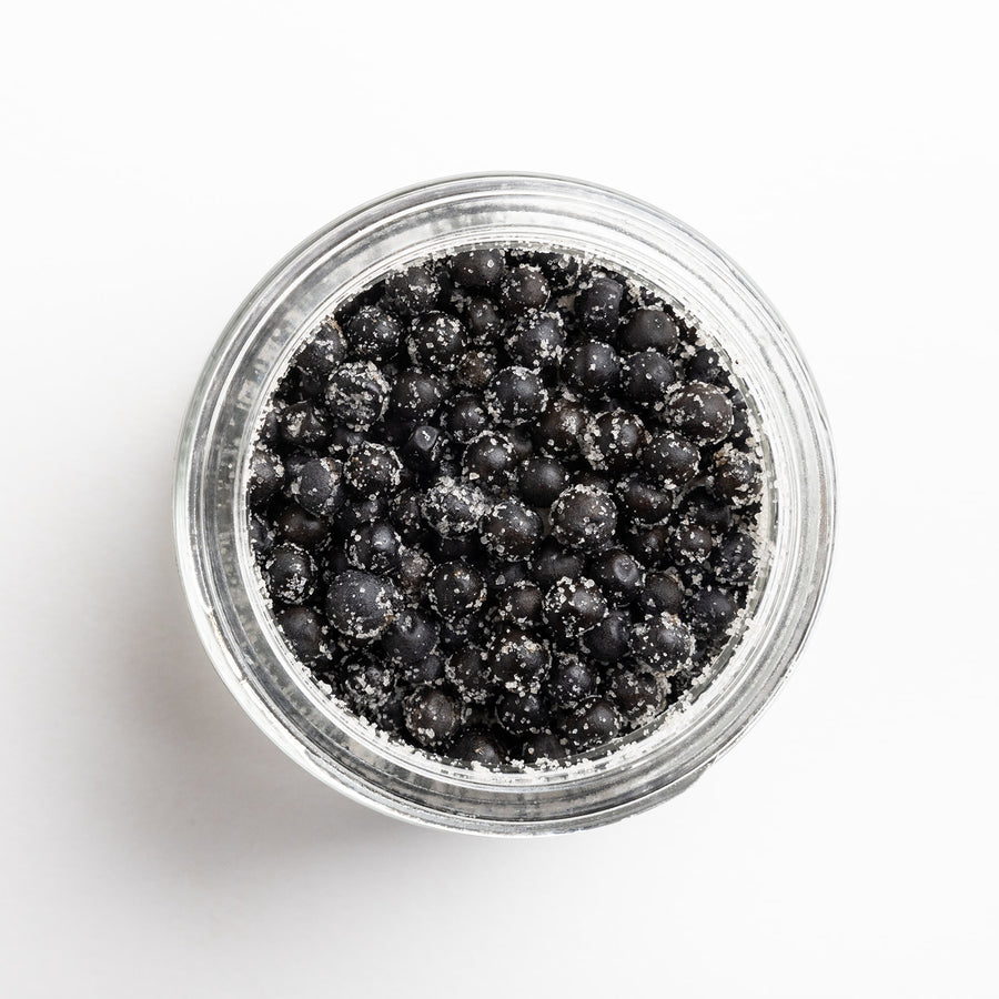 Clear jar filled with black peppercorns on a white background