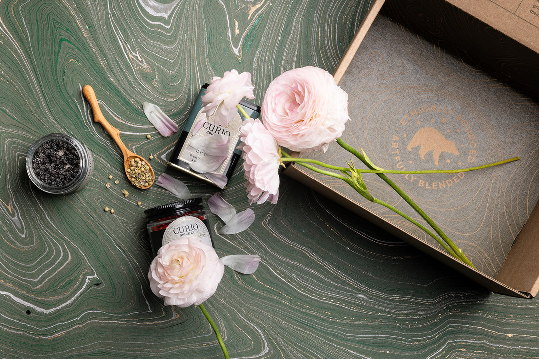 Spices artfully displayed on a marbled green background with flowers and a shipping box.