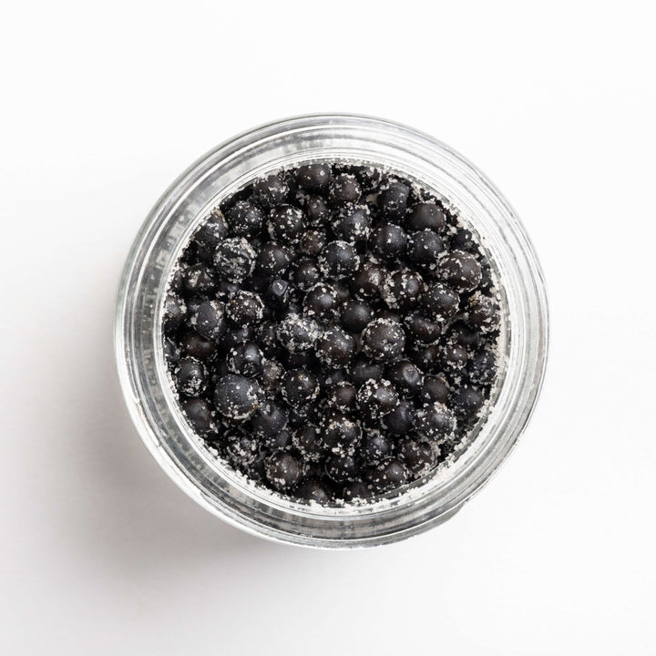 Clear jar filled with black peppercorns on a white background