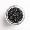 Clear jar filled with black peppercorns on a white background