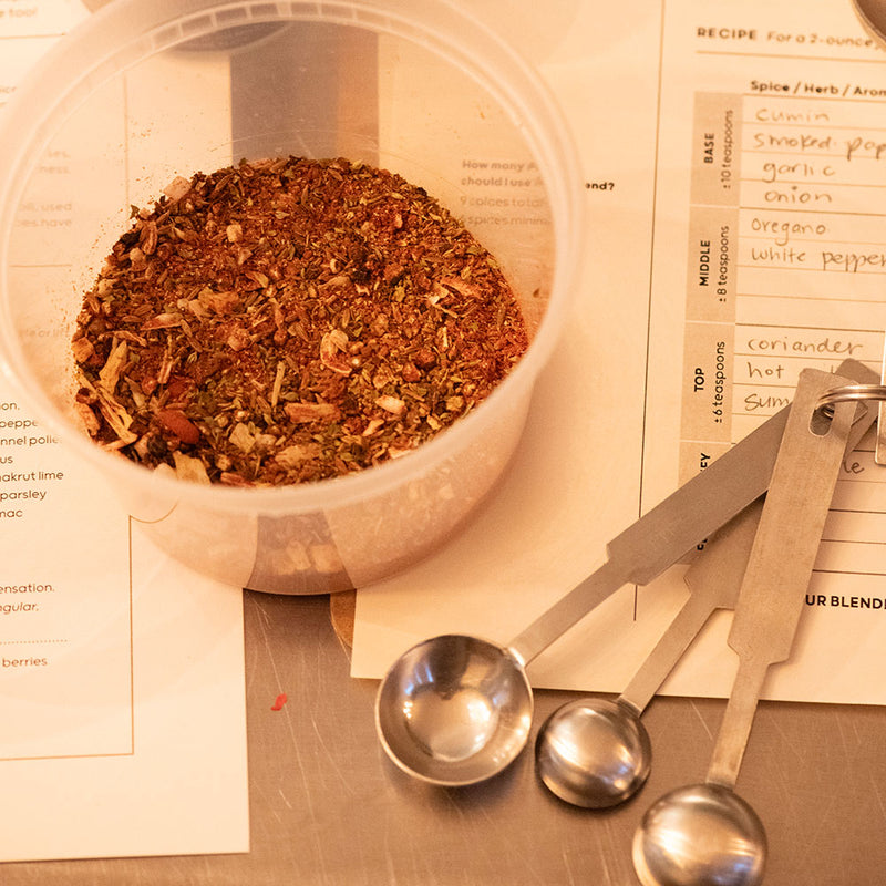 A blend in a plastic jar next to measuring spoons and notes from Curio's Spice Blending classes