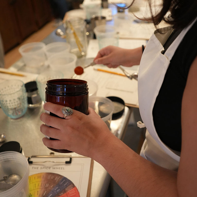 Spooning spices into a jar during Curio's Spice Blending class