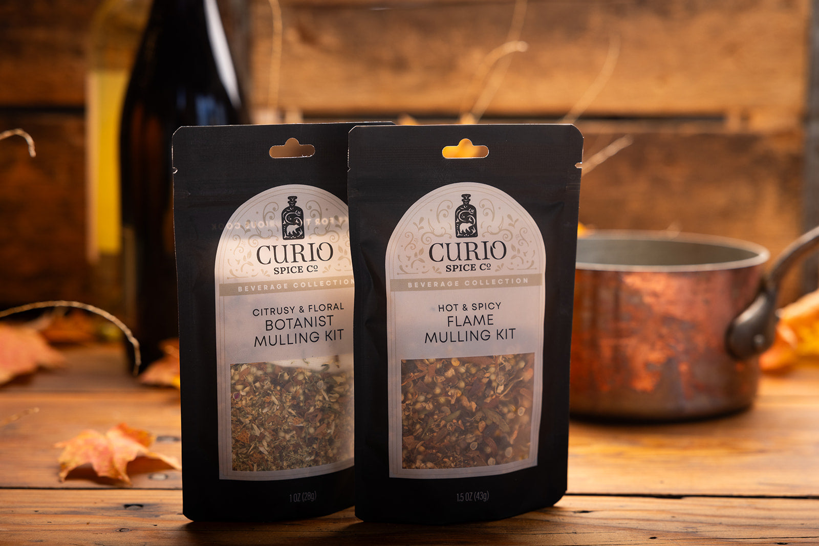 Two Curio Spice Co. mulling kit packages on a wooden surface with a kitchen background.