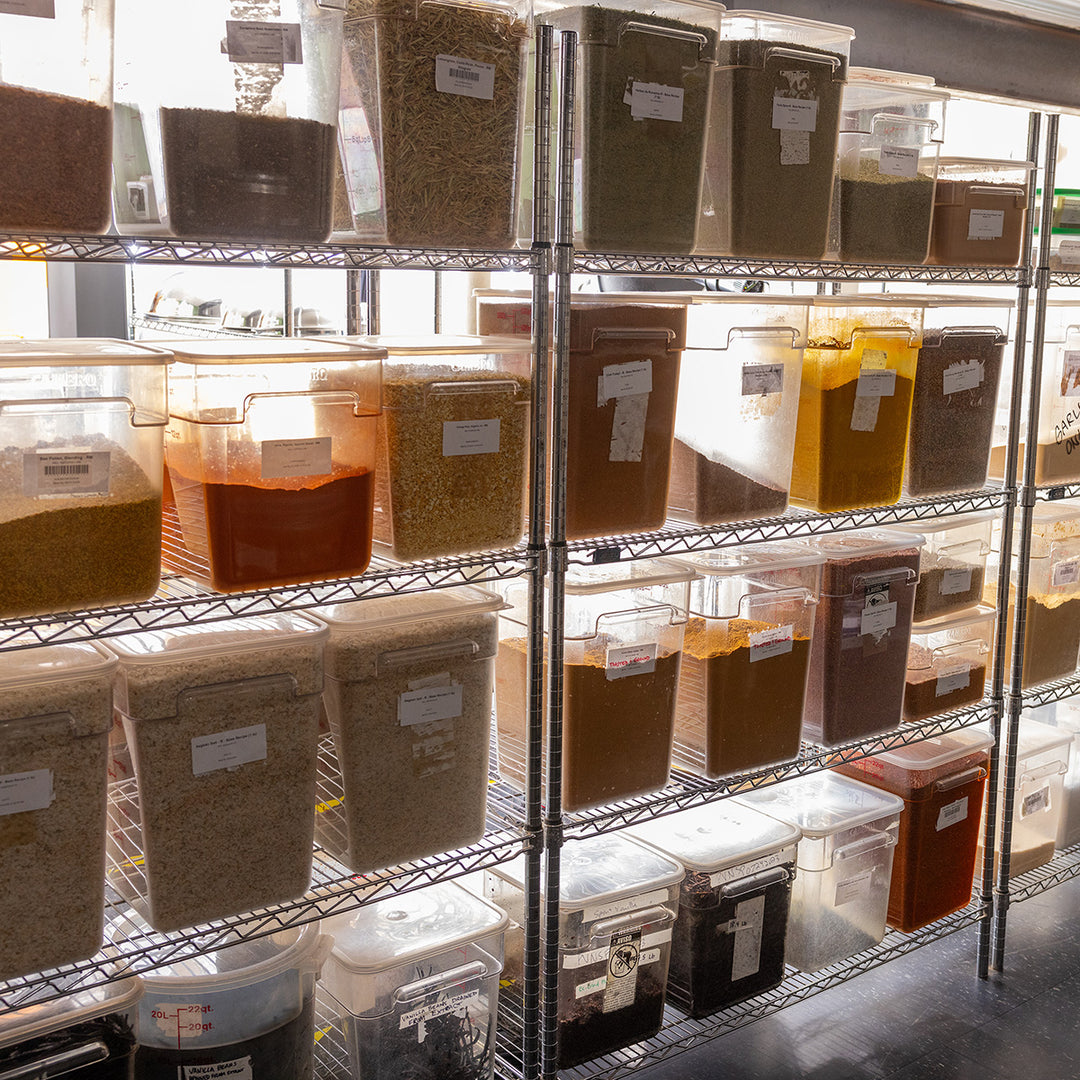 Shelves with labeled containers holding various spices in a storage room.