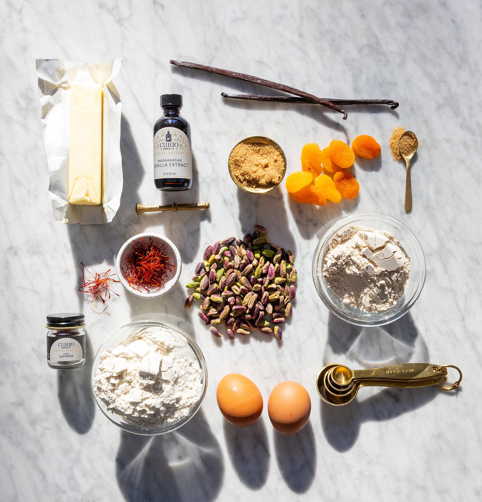 Ingredients for baking including flour, eggs, spices, and vanilla extract on a marble surface.