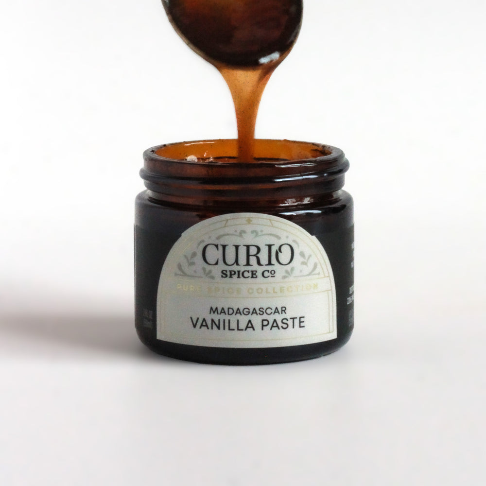 A spoon dipping into a jar of Curio Spice's Madagascar Vanilla Paste.